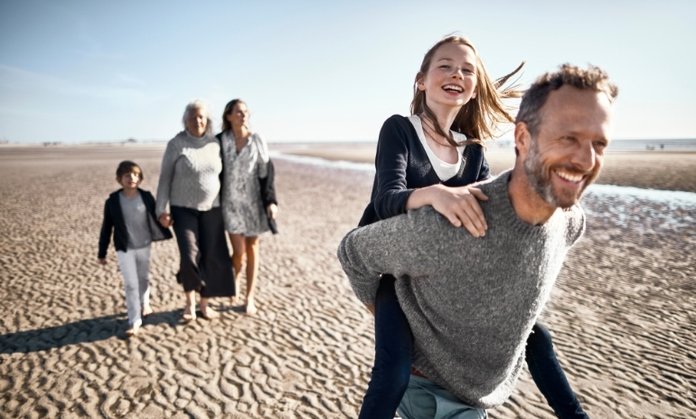 Happy family on the beach, girl on man's back, in the background two women and another child