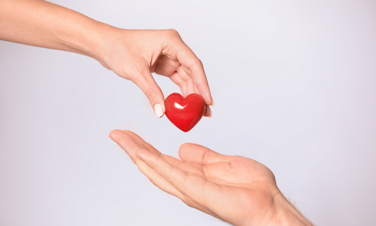 Woman giving red heart to man on white background