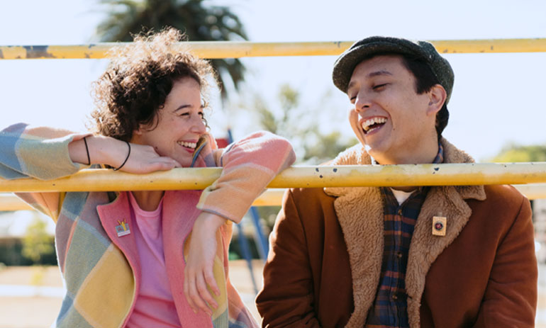 Prue and her partner wearing coloured clothing entwined in playground equipment and laughing.