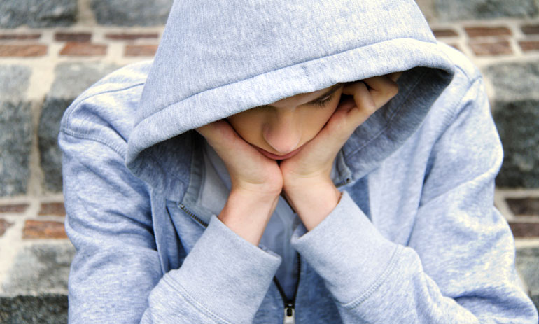young teenager in grey hoodie looking sad