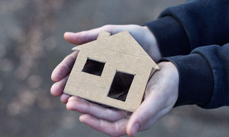 young homeless boy holding a cardboard house