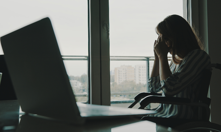 Person with disability sitting by laptop with head in hands