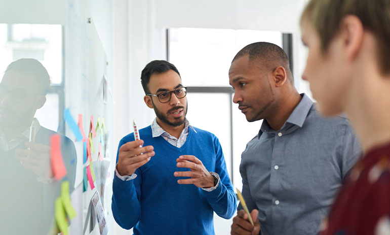 three people standing, strategising on a whiteboard