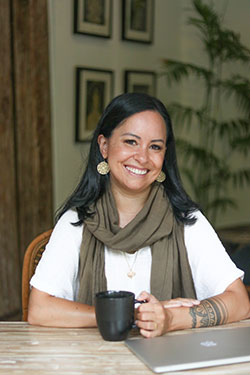 Jackie Hanafie. Smiling woman wearing white top sitting at a table holding a cup