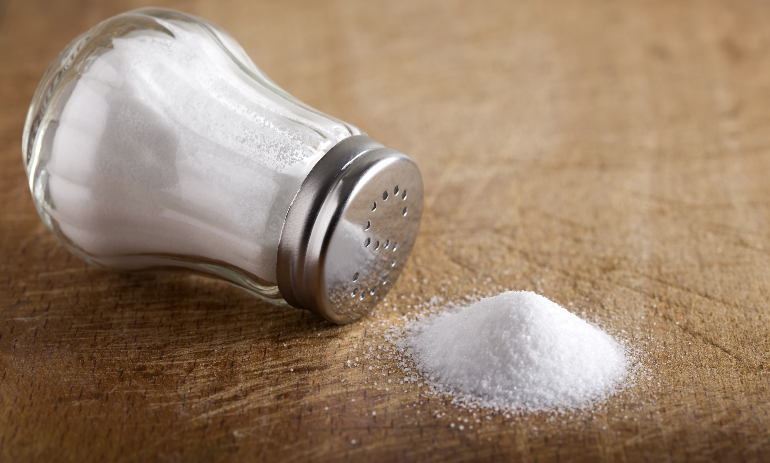 Traditional glass salt cellar and spilled salt on a wood background