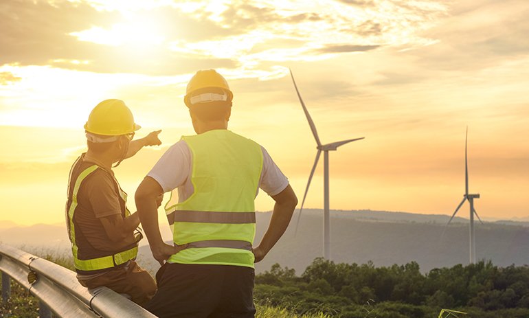 two engineers wearing hi vis vests looking at wind turbines