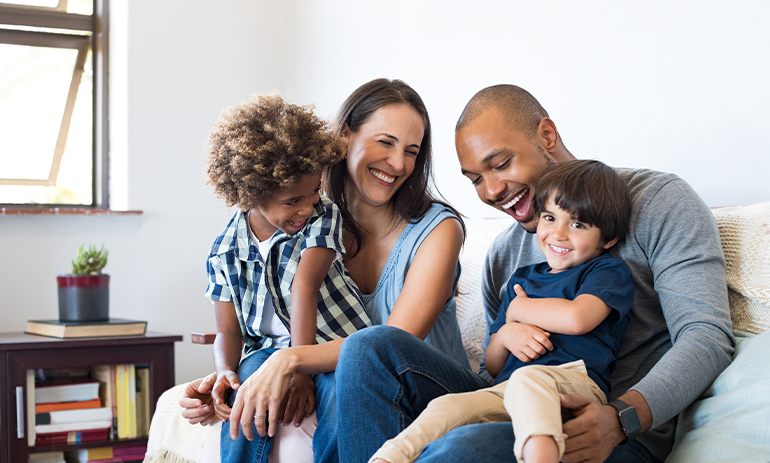 Parents with two children sit laughing on a couch