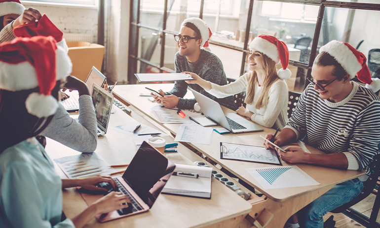 group of people sat around a table working wearing Santa hats