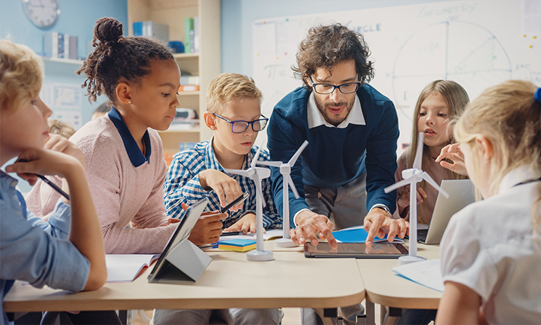 A teacher leans over a desk with a group of kids