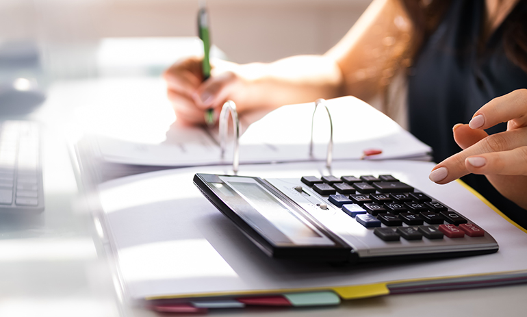 close up of woman typing in a calculator with a pen in her other hand