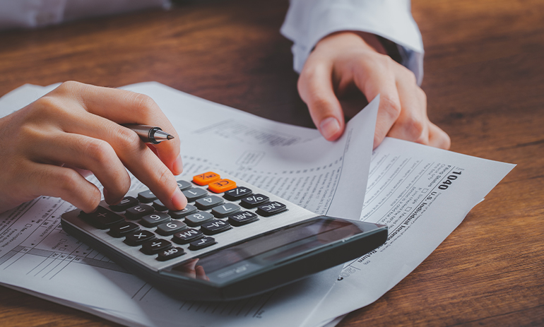 close up paper work and person putting numbers into a calculator