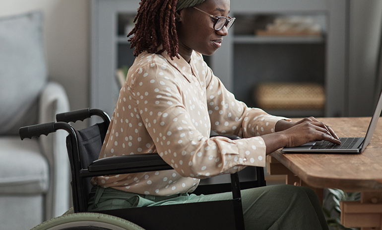 black woman in wheelchair at table working on laptop