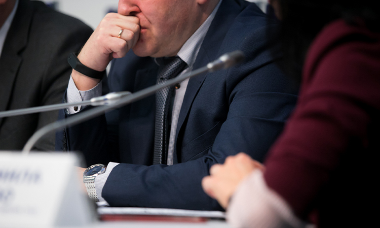 close up man in suit sitting in front of microphone on a panel