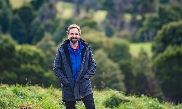 Ryan Swenson stands in a field with trees in the background