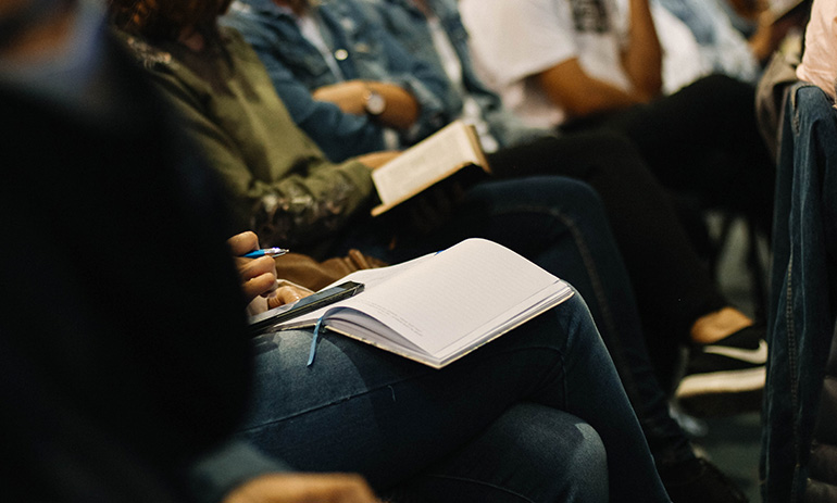 A crowd sits with empty notebooks on their laps at an event