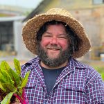 Headshot of Josh Collings, founder of Acres and Acres, standing in a garden wearing a straw hat