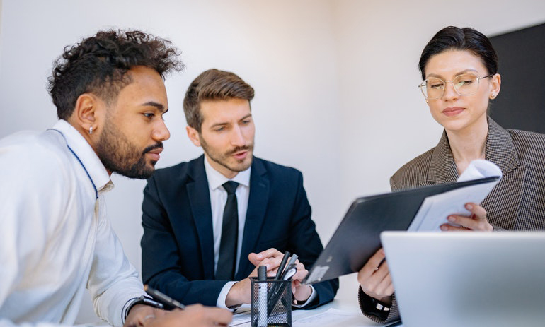 Three people sitting at a table looking at a clipboard